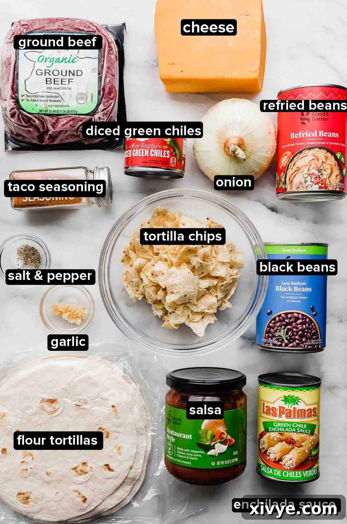 An image showing the ingredients needed for Mexican lasagna, including ground beef, cheese, green chilies, onion, refried beans, taco seasoning, garlic, tortillas chips, black beans, salsa, tortillas, and enchilada sauce!