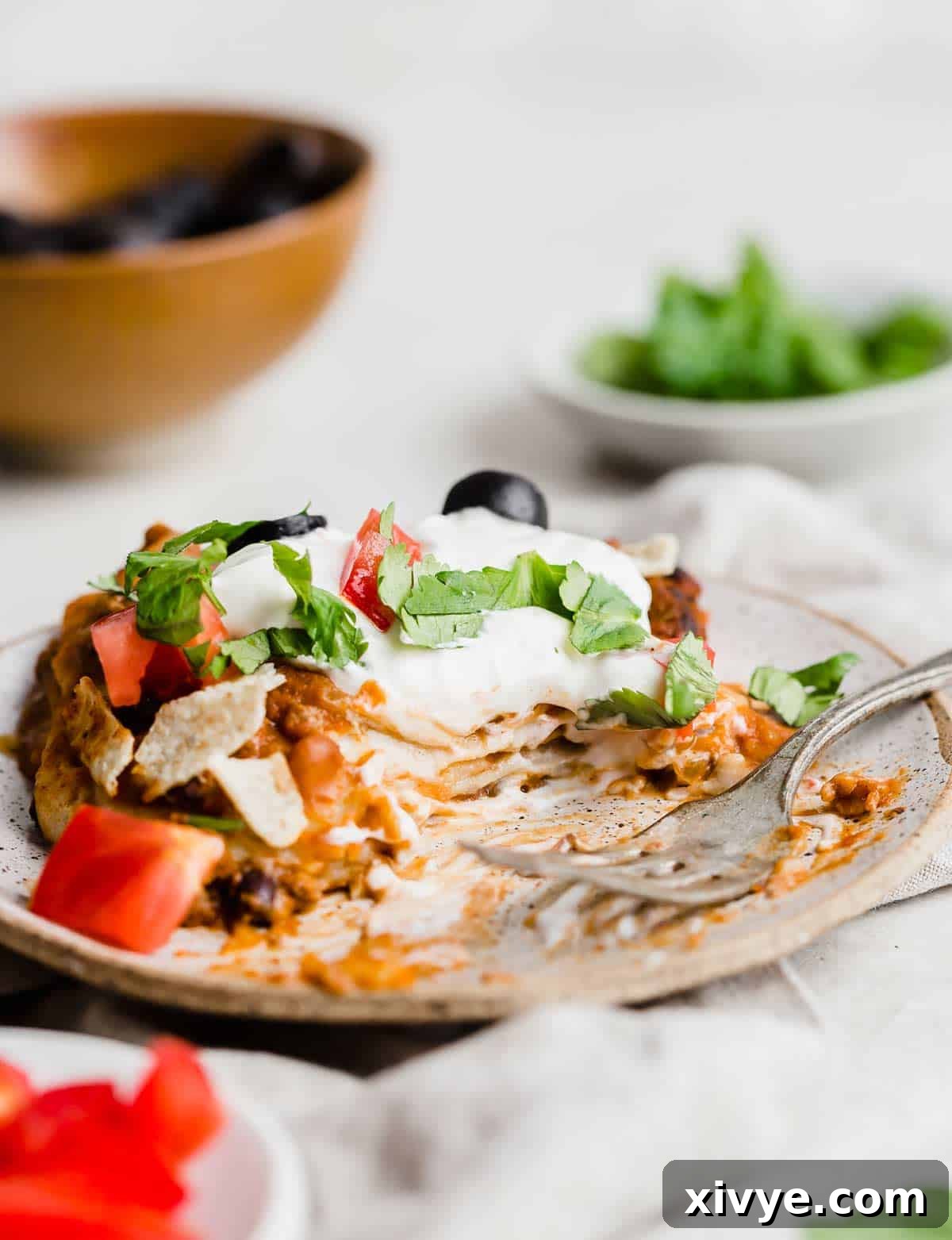 Mexican Lasagna made with flour tortillas and topped with olive, sour cream, tomatoes, and lettuce on a plate.