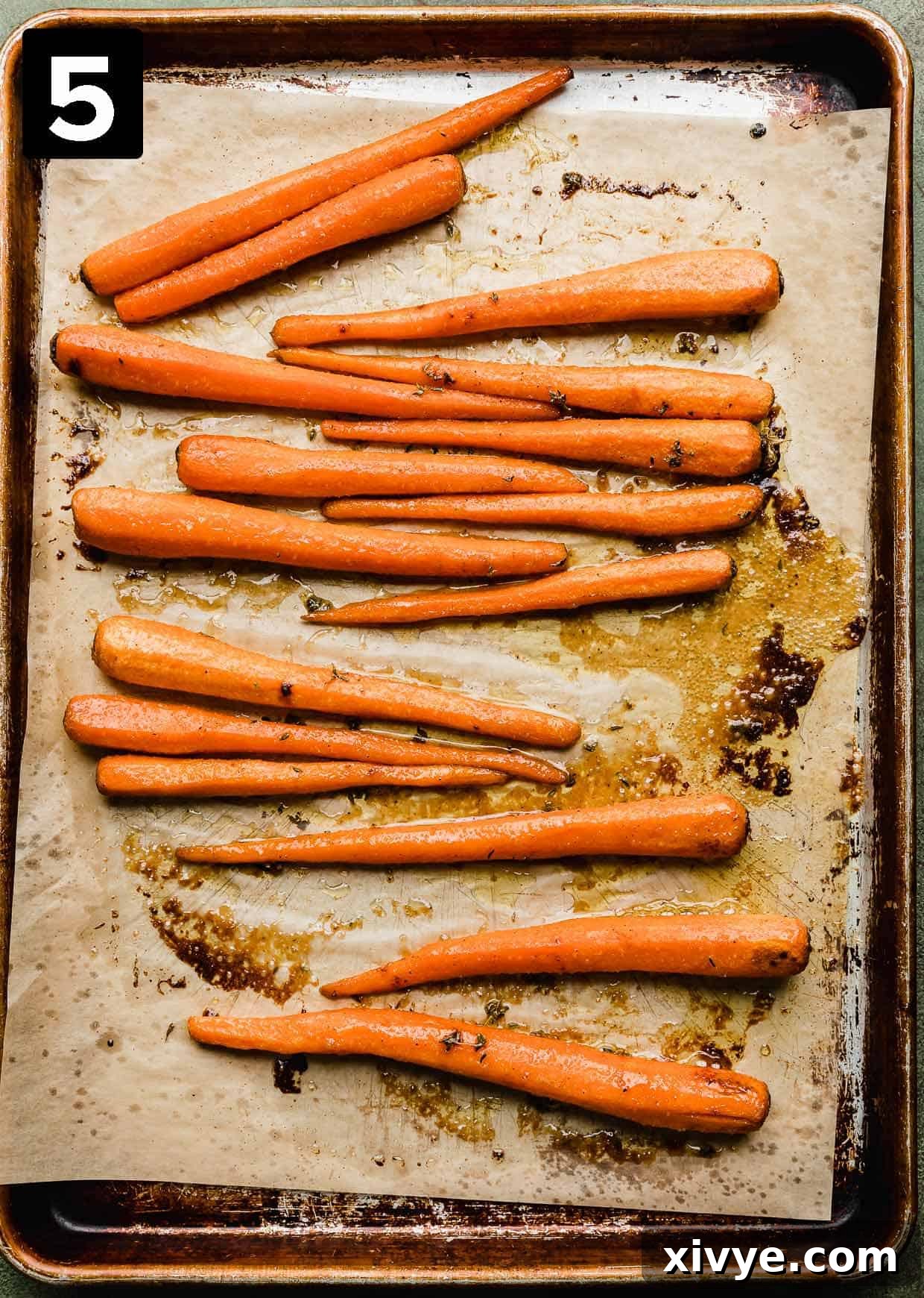 A close-up shot of perfectly golden-brown, caramelized brown sugar roasted carrots spread out on a parchment-lined baking sheet, fresh out of the oven.