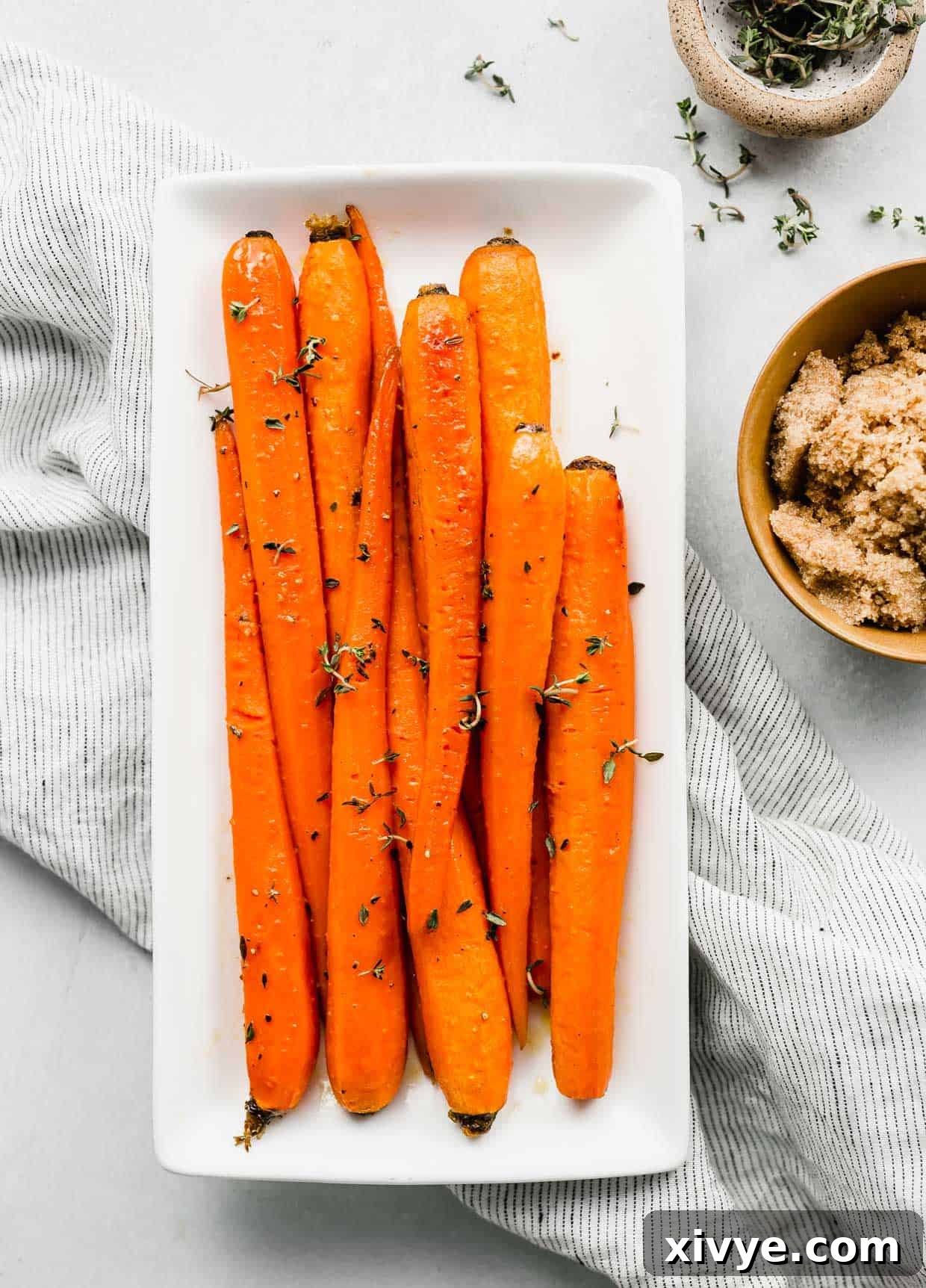 Beautifully roasted brown sugar carrots, garnished with fresh thyme, presented on an elegant white rectangular serving plate.