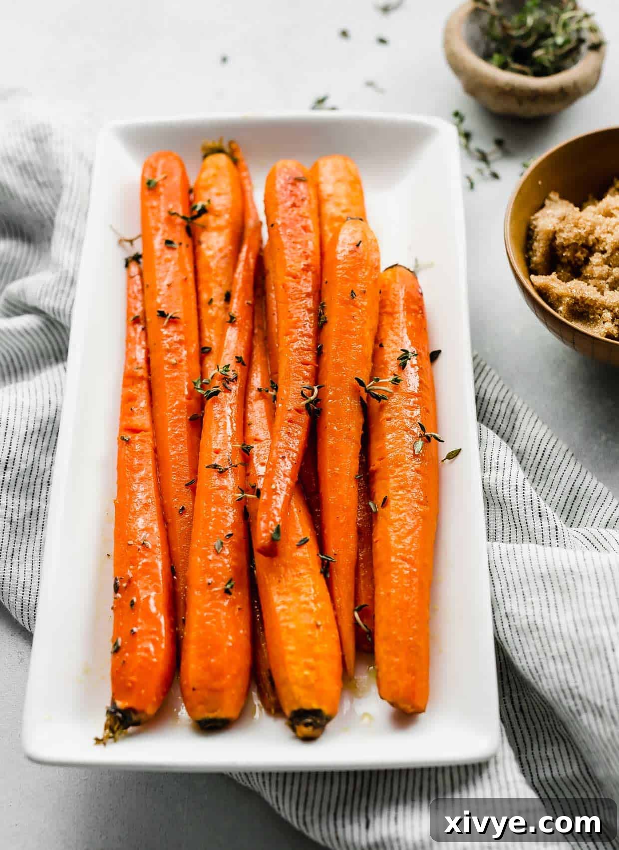Close-up of perfectly glazed brown sugar roasted carrots topped with fresh thyme, presented on a white serving plate, highlighting their appetizing shine.