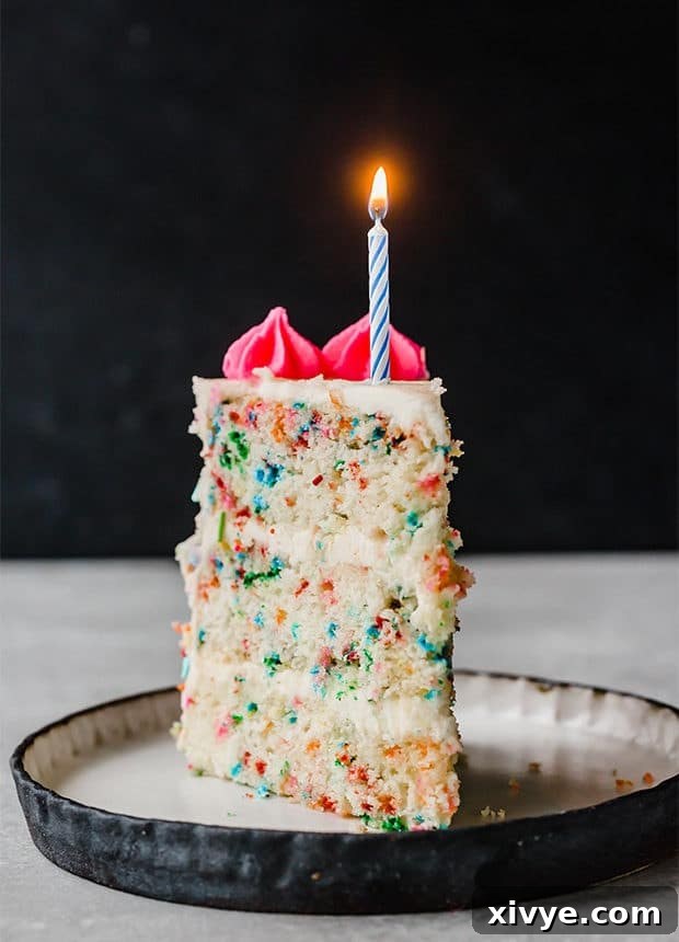 A slice of Funfetti Cake with one candle lit on the top of the cake slice.