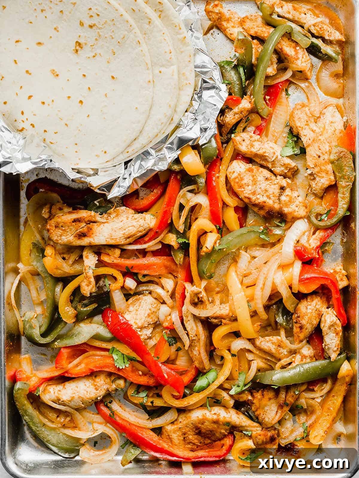 A baking sheet with cooked sliced peppers, chicken, and onions on it, fresh out of the oven.