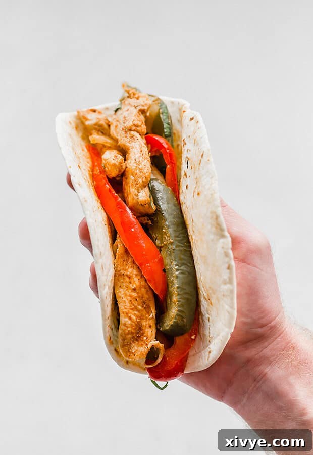 A hand holding a flour tortilla loaded with savory chicken fajitas.