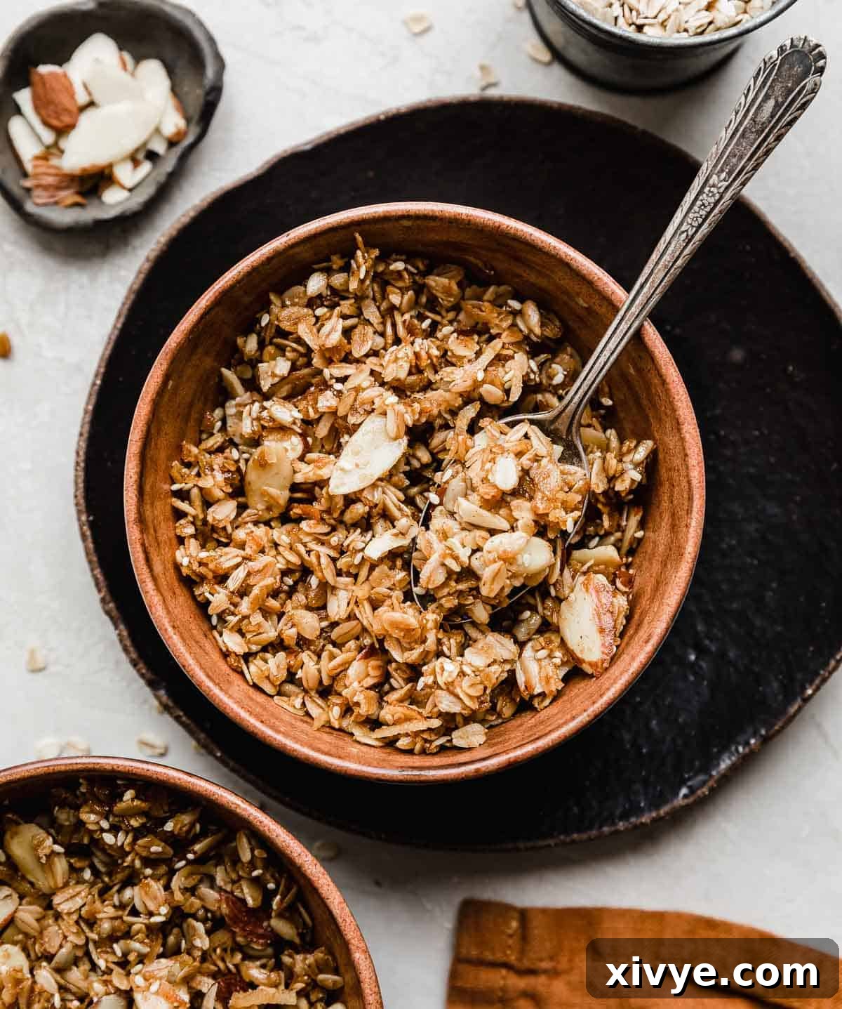 A Granola Recipe with sliced almonds and sweetened coconut in a brown bowl on a light gray textured background.