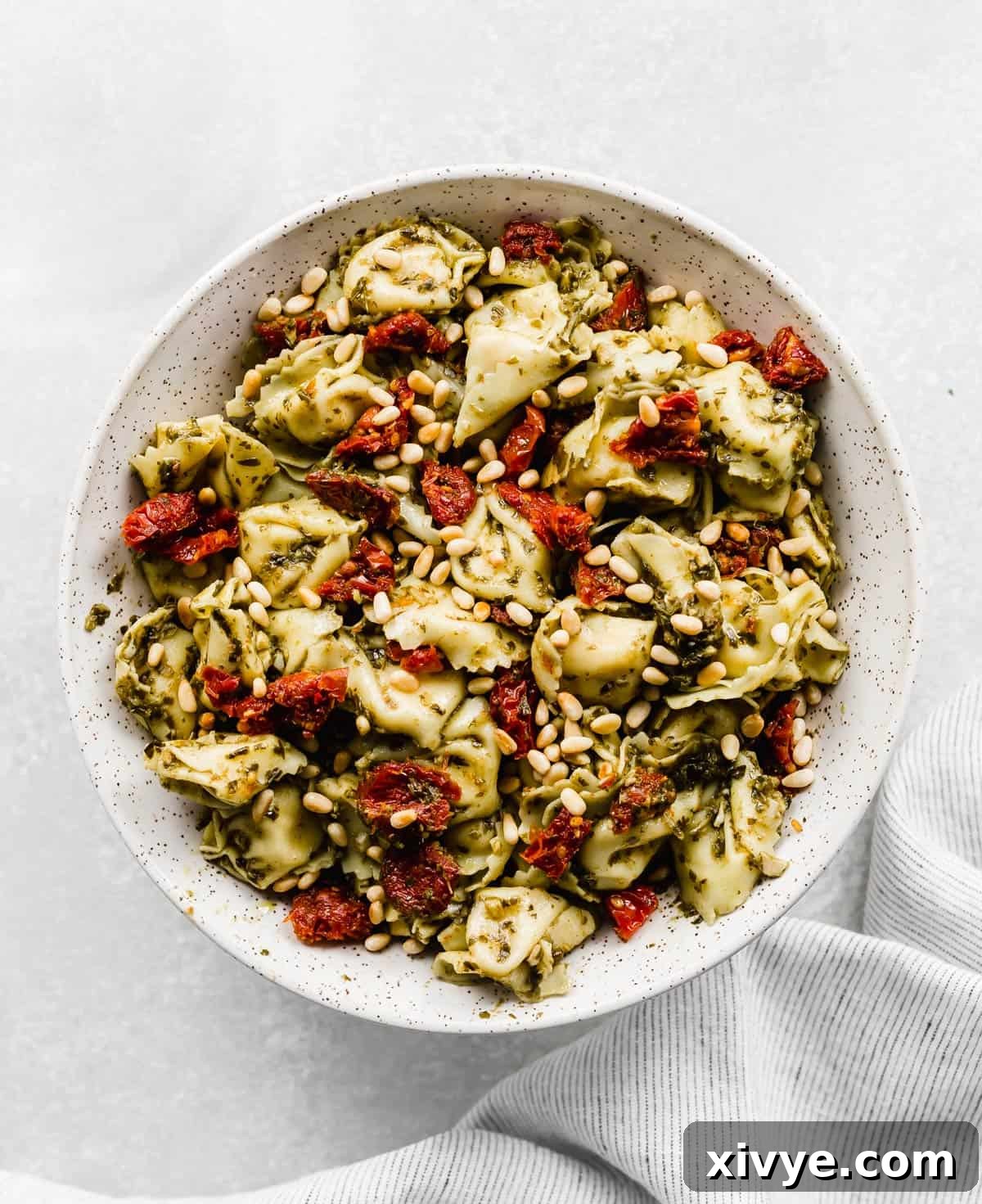 A large bowl with Pesto Tortellini Pasta Salad with pine nuts and sun-dried tomatoes.
