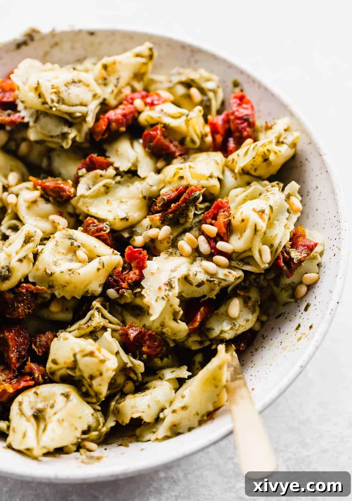 A close up photo of Pesto Tortellini Pasta Salad with sun-dried tomatoes and pine nuts in the salad. 