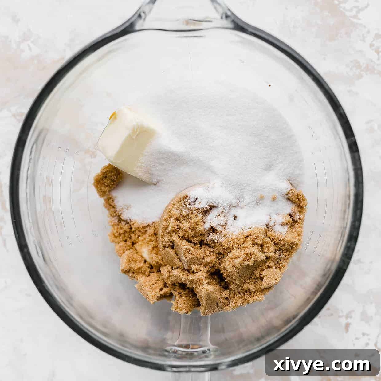 A vibrant mix of brown sugar, granulated sugar, and softened butter inside a clear glass mixing bowl, ready for creaming.