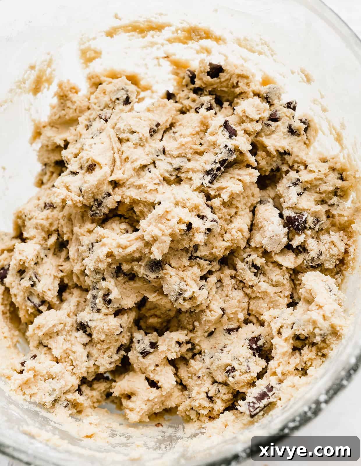 Thick, rich chocolate chip cookie dough batter, laden with various types of chocolate, ready for chilling.
