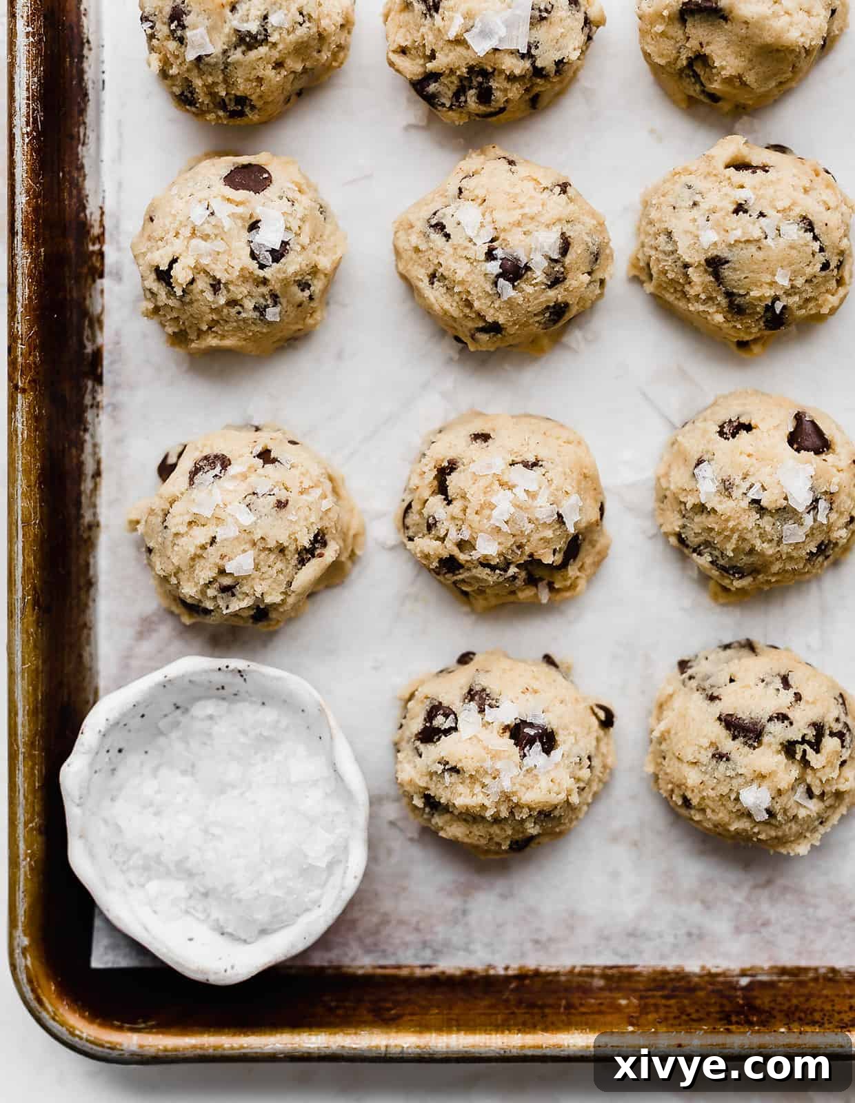 Perfectly scooped chocolate chip cookie dough balls, topped with flaky sea salt, arranged on a parchment-lined baking sheet.