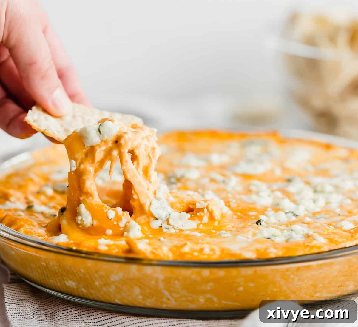 The Ultimate Buffalo Chicken Dip 2 A crisp tortilla chip perfectly scooping a generous portion of creamy Buffalo Chicken Dip with visible blue cheese crumbles on top.