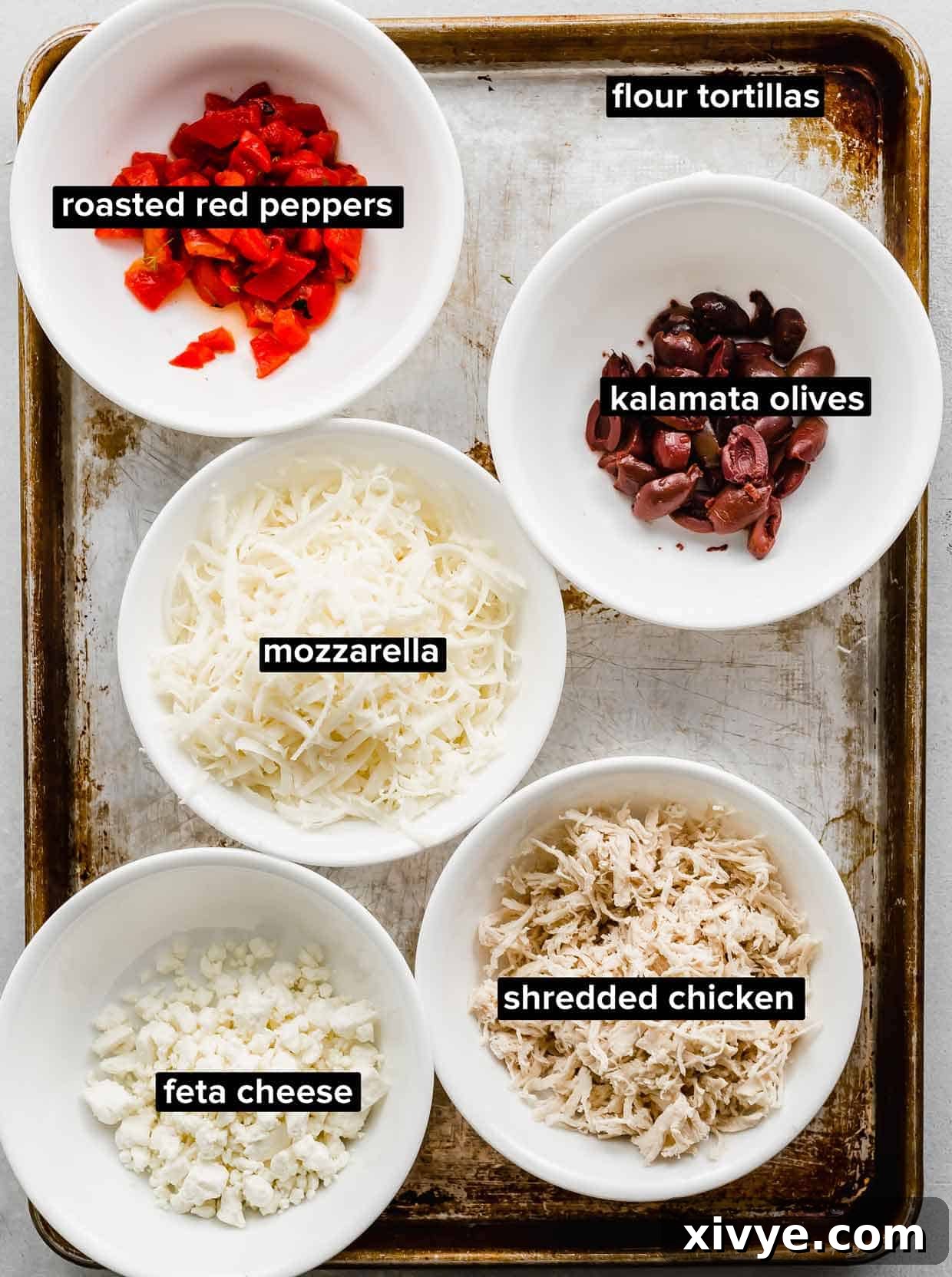 Ingredients used to make Greek Quesadillas portioned into white bowls on a seasoned baking sheet.
