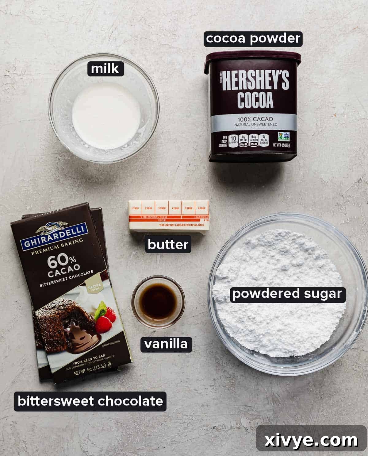 Chocolate cake pop frosting ingredients on a gray background: bittersweet chocolate, powdered sugar, butter, milk, and cocoa powder.