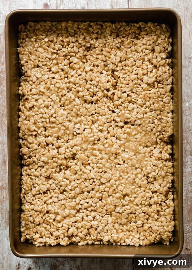 A casserole dish filled with the pressed Rice Krispies and peanut butter base for Scotcharoos.