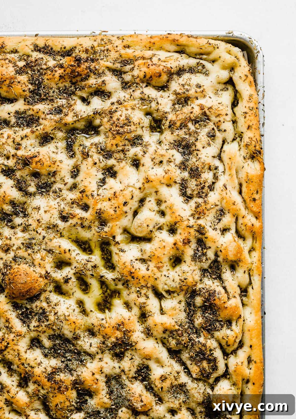 Easy Focaccia Bread baked to a beautiful golden brown on a baking sheet, generously topped with an abundance of fragrant fresh herbs.