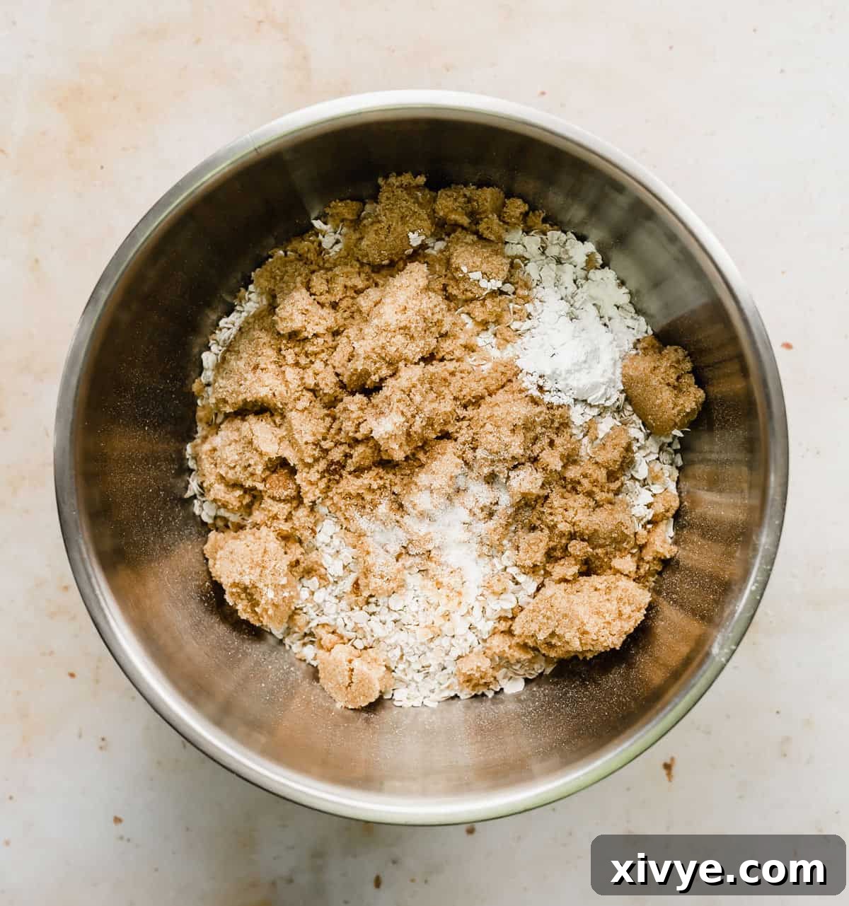 A metal bowl full of the dry ingredients used to make a baked oatmeal cake recipe, perfectly mixed and ready for the wet components.