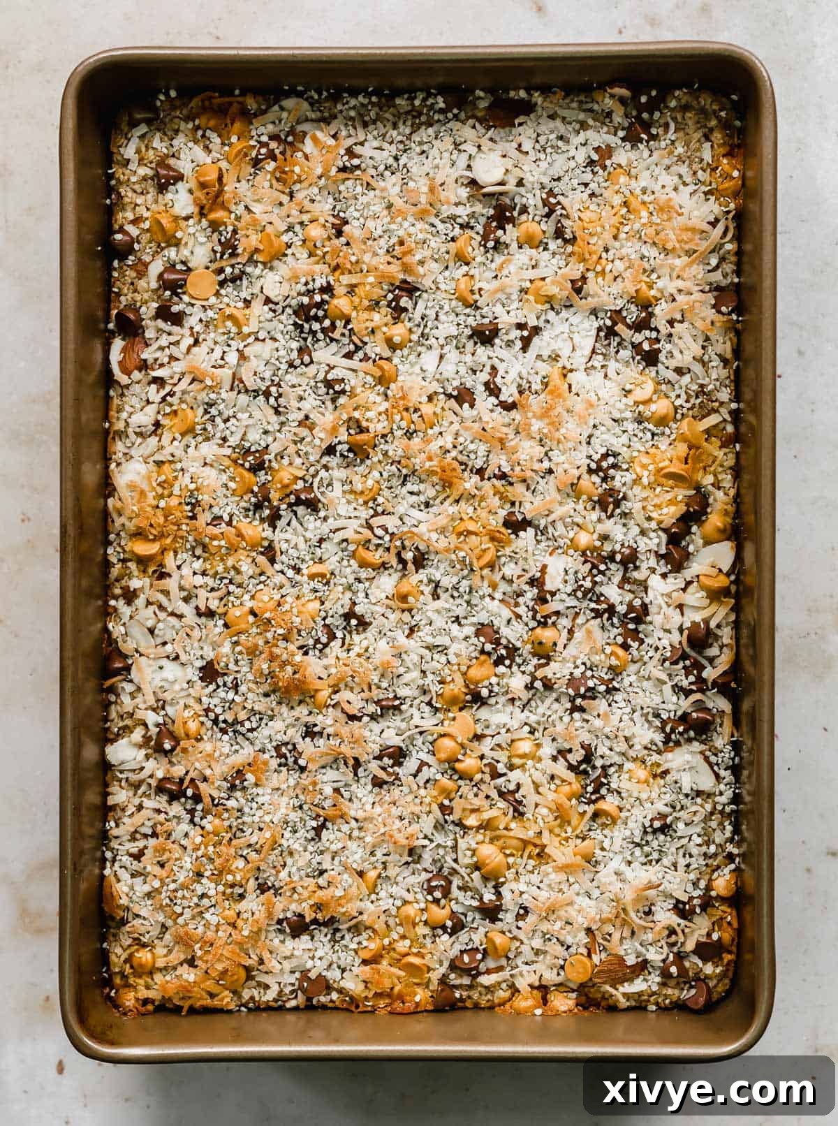 A Breakfast Baked Oatmeal Cake in a rectangular baking dish, richly topped with toasted coconut, chocolate chips, hemp hearts, and butterscotch chips, ready to be served.