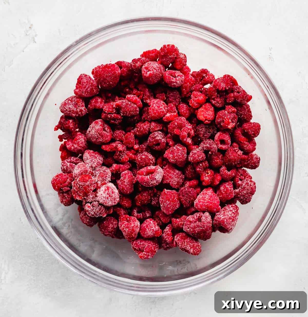 No-Fuss Raspberry Freezer Jam 4 Frozen raspberries in a glass bowl on a white background.