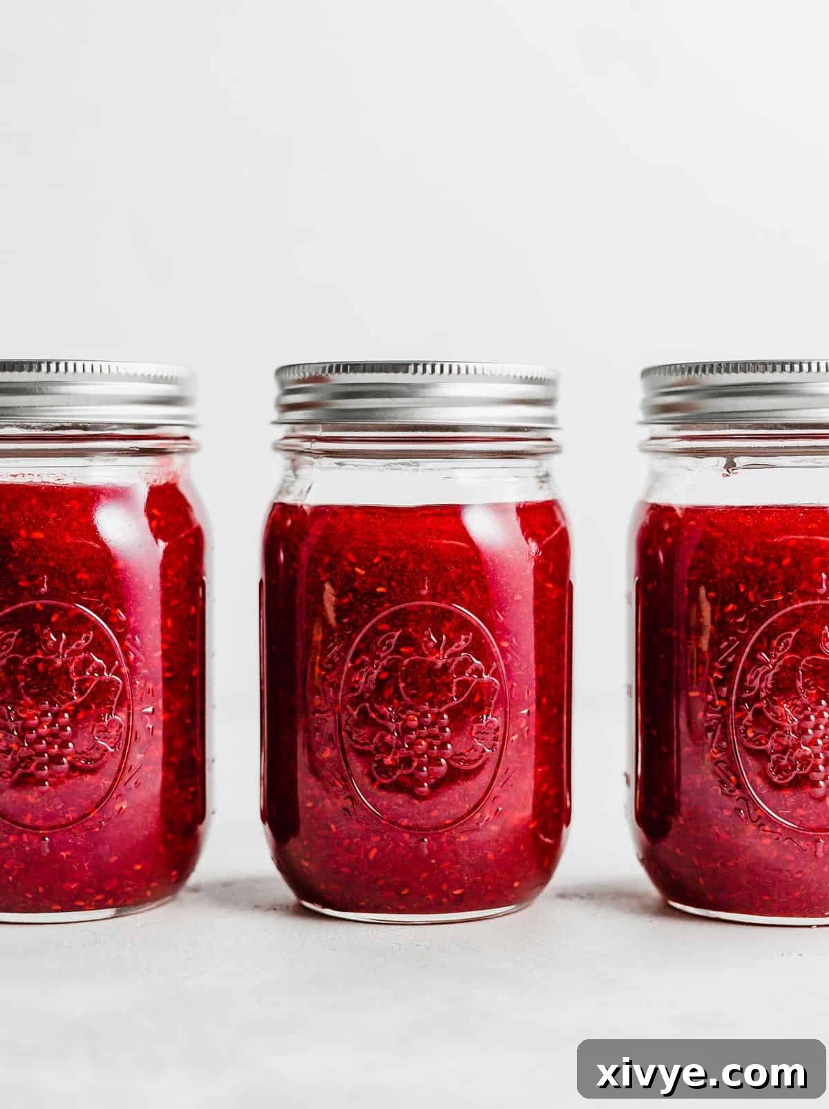 No-Fuss Raspberry Freezer Jam 8 Three jars of Raspberry Freezer Jam on a white background.