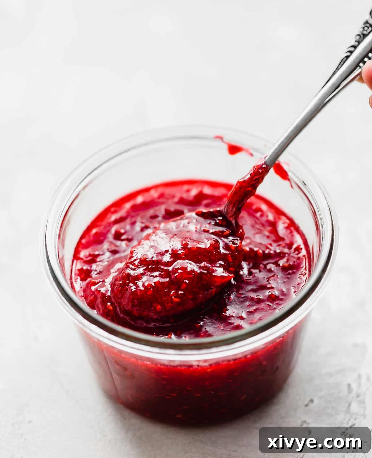 No-Fuss Raspberry Freezer Jam 10 A glass jar filled with Raspberry Freezer Jam and a spoon scooping some out.