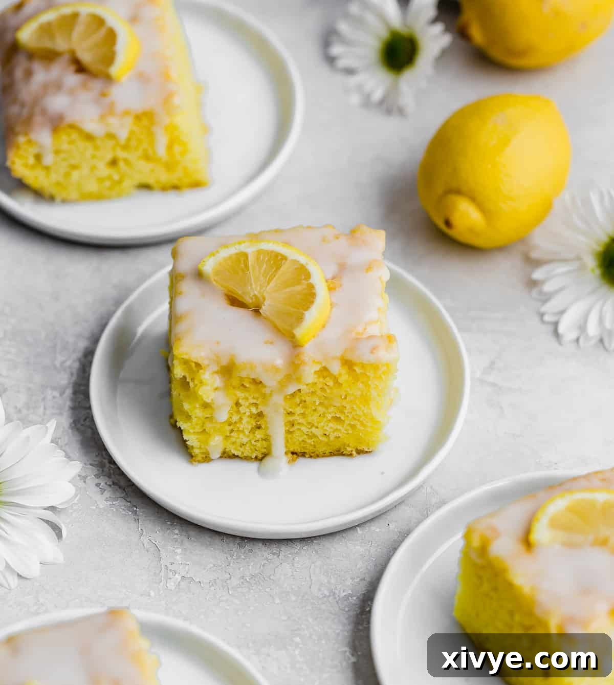 A perfectly square slice of Lemon Jello Cake on a pristine white plate, elegantly garnished with a fresh lemon wedge.