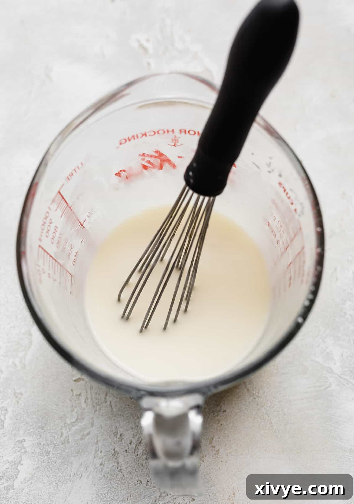 A creamy white glaze mixture, enriched with lemon, filling a liquid measuring cup, ready to adorn the cake.