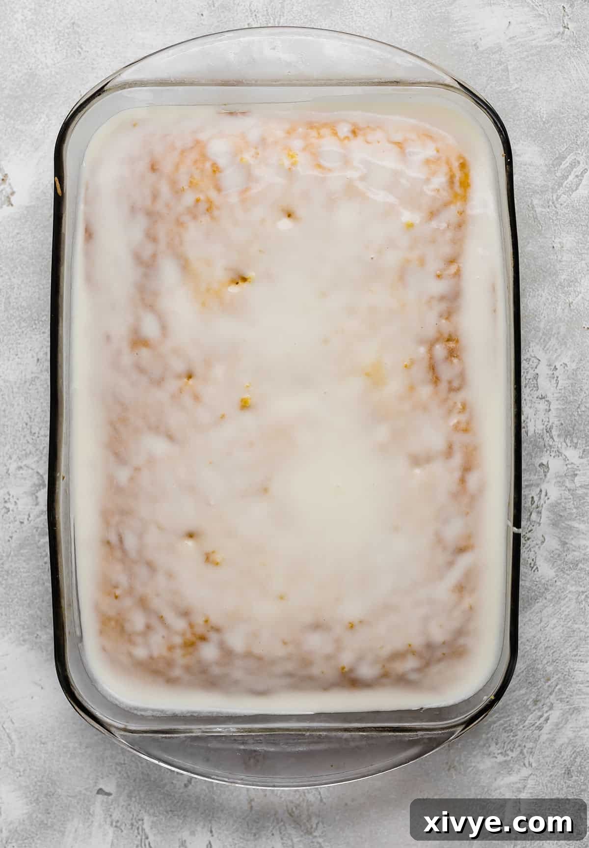 A pristine white glaze generously covering a lemon cake, still in its rectangular glass dish, promising a sweet, tangy experience.