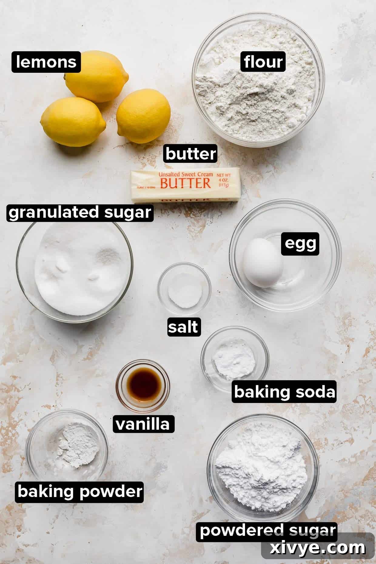 Lemon Cookies ingredients portioned into glass bowls on a white textured background.
