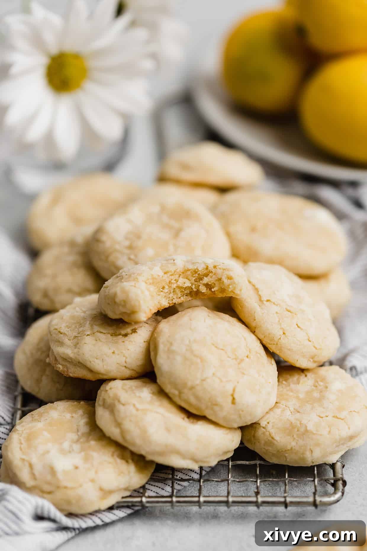 A lemon cookie with a bite taken out of it, stacked on a pile of other baked lemon cookies.