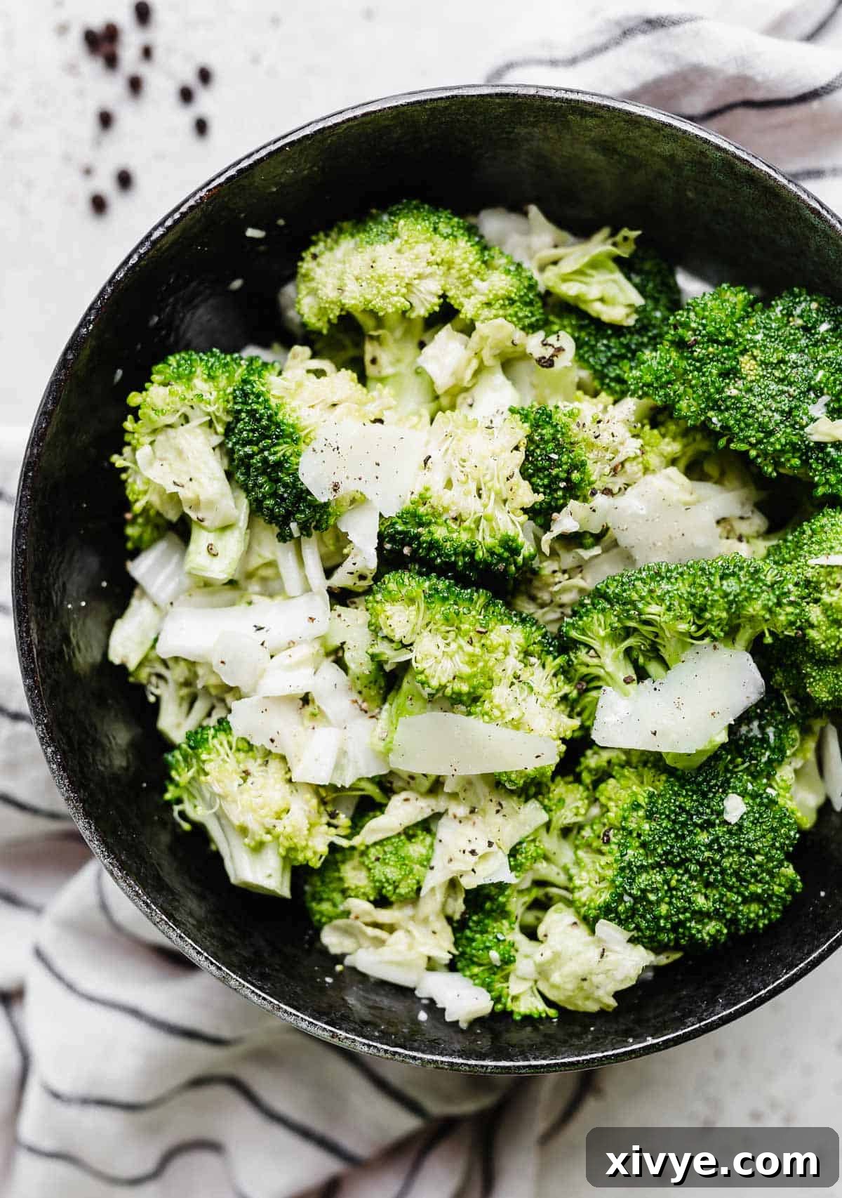 A vibrant Broccoli Caesar Salad in a sleek black bowl, generously garnished with freshly shaved parmesan, highlighting its appealing crunch and rich texture.