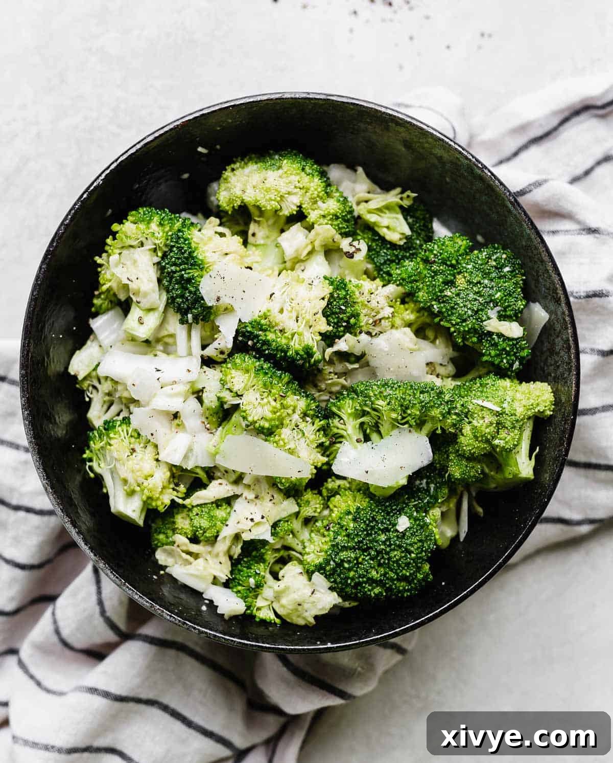 A beautifully presented Broccoli Caesar Salad with tender Napa cabbage in a black bowl, set against a sleek light gray background, ready to be enjoyed.