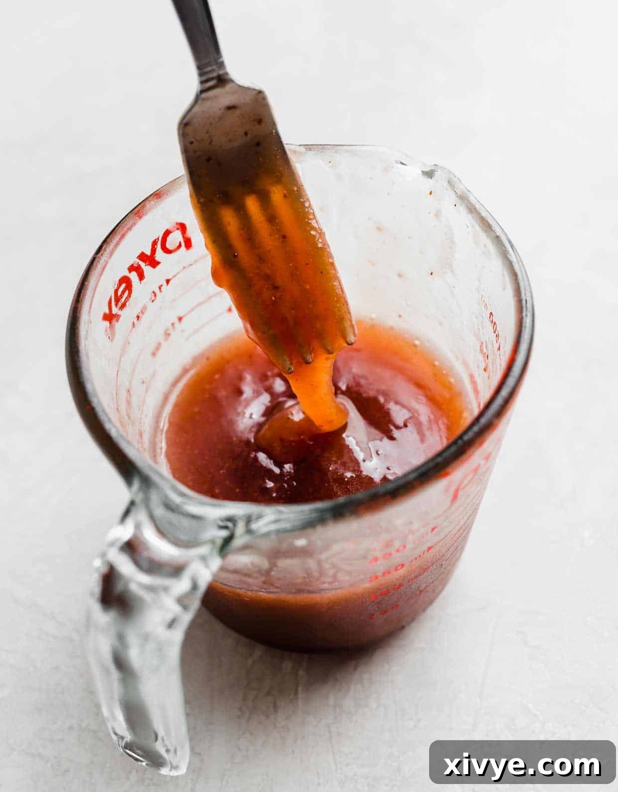 A homemade strawberry vinaigrette dressing in a clear glass measuring cup, set against a pristine white background. The dressing appears smooth and creamy, showcasing its rich texture.