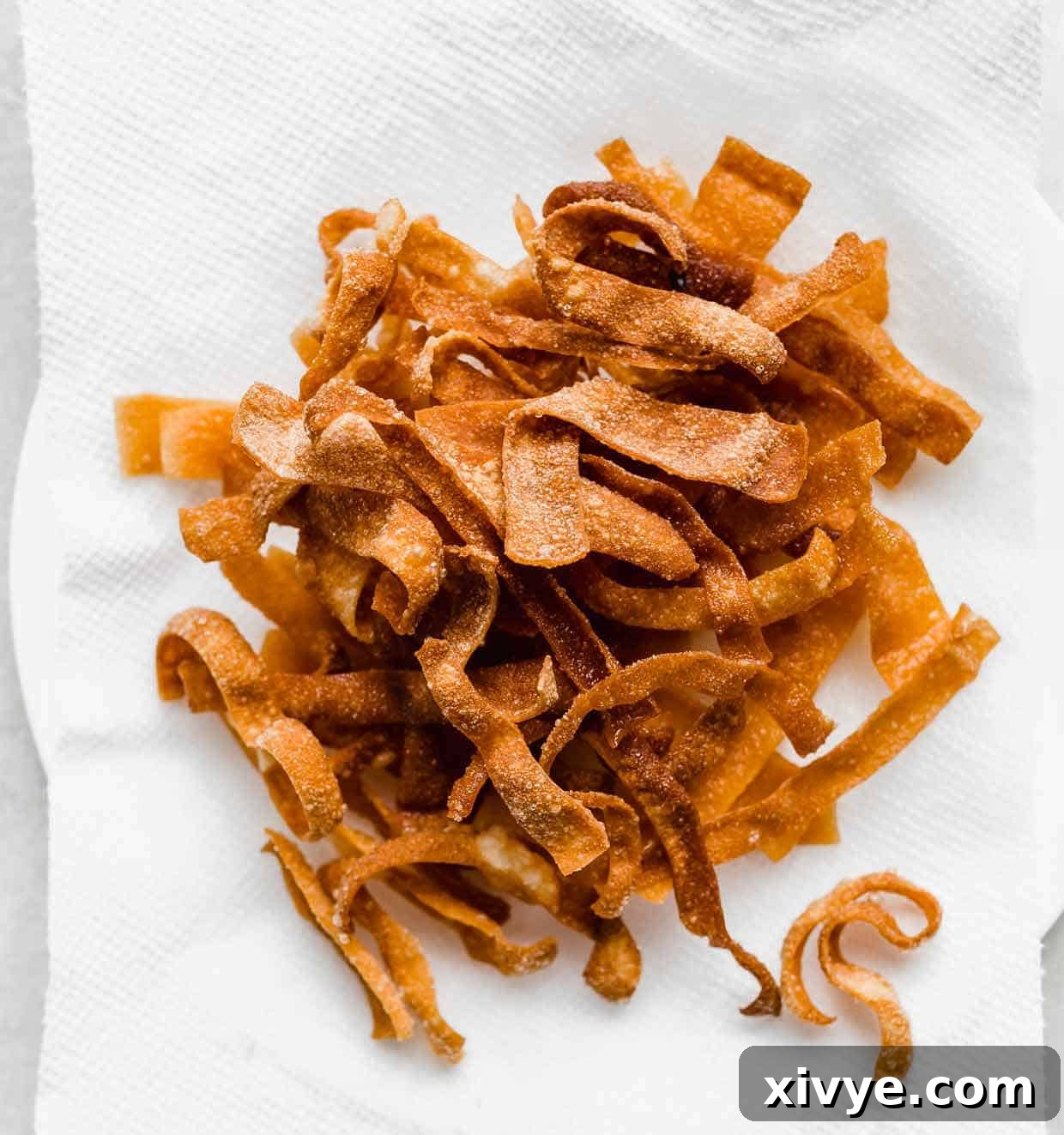 A pristine white paper towel holding an arrangement of golden brown fried wonton strips, effectively draining any residual cooking oil.