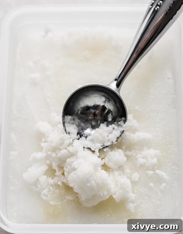 An ice cream scoop digging into a large container of frozen limeade, ready to be scraped for slush.