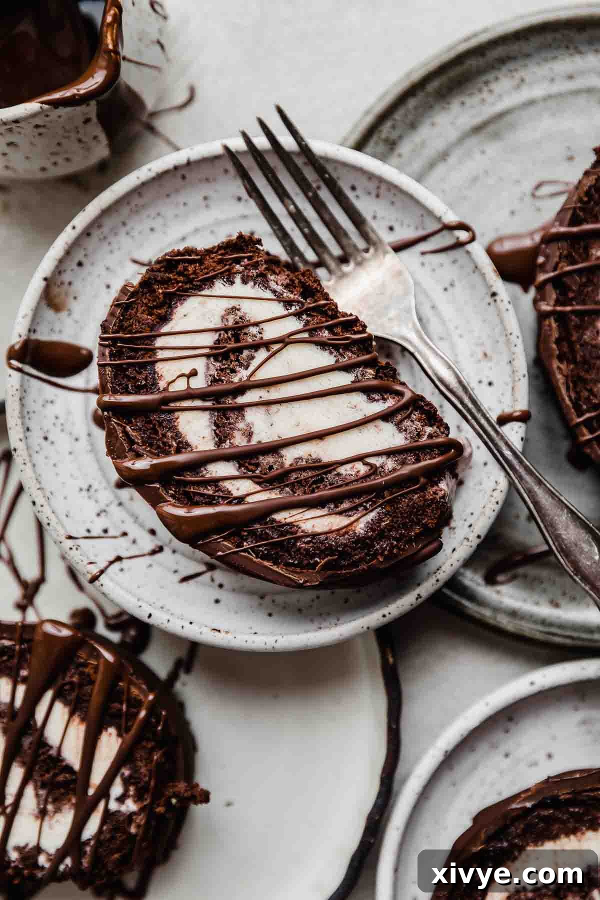 A slice of a perfectly swirled Ice Cream Cake Roll on a white plate, with a metal fork resting beside it, ready to be enjoyed.