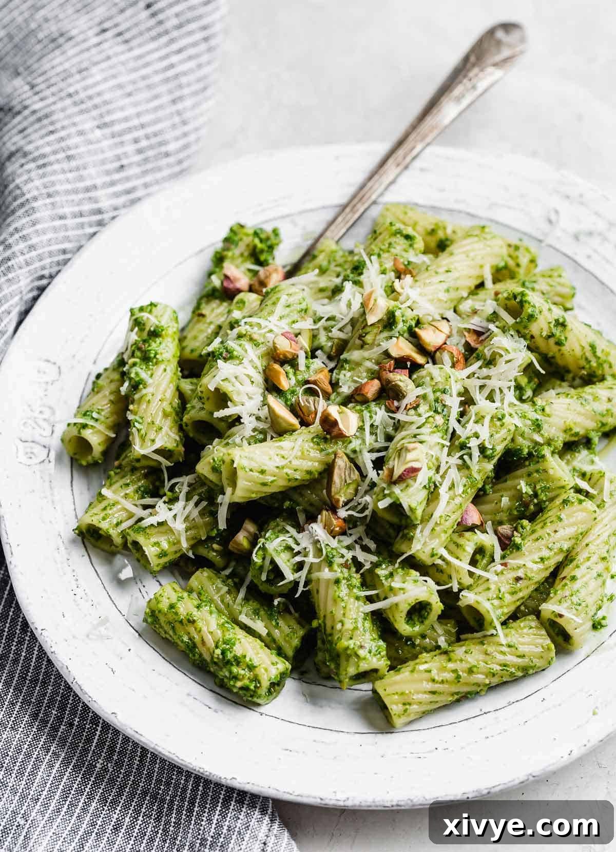Vibrant Kale Pesto Pasta with rigatoni noodles on a pristine white plate, garnished with fresh herbs and cheese.