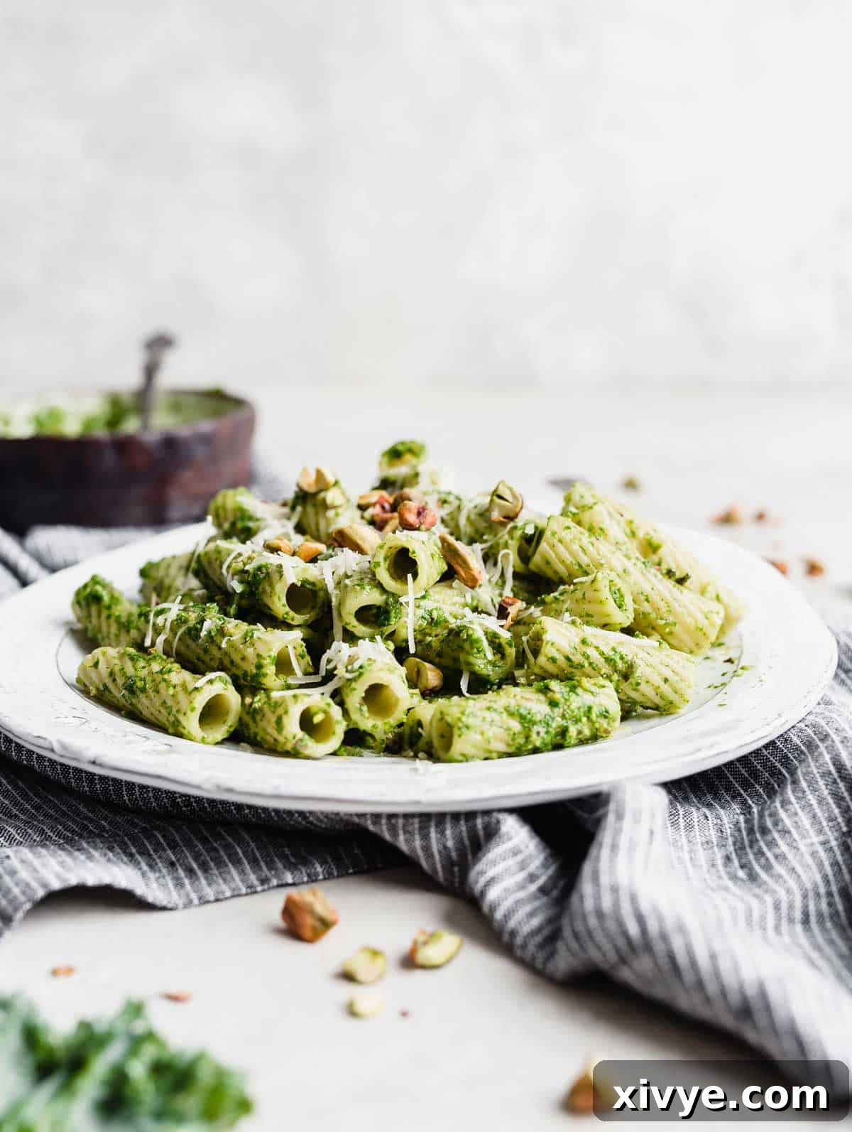 Close-up of Rigatoni Kale Pesto Pasta on a white plate, showcasing the rich green sauce and garnishes against a clean white background.