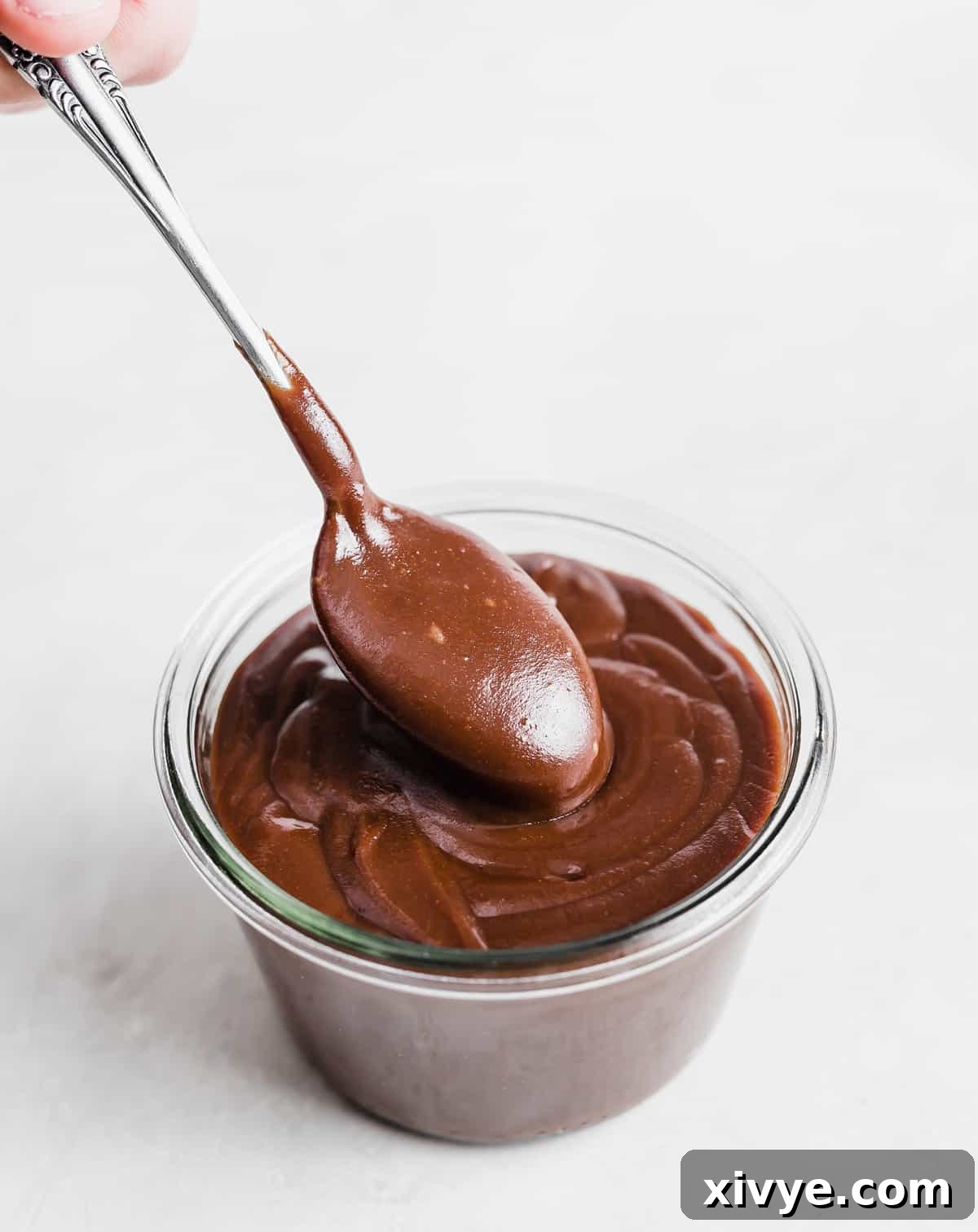 Classic Hot Fudge Sauce 10 A spoon lifting out a portion of homemade Hot Fudge Sauce from a glass cup.