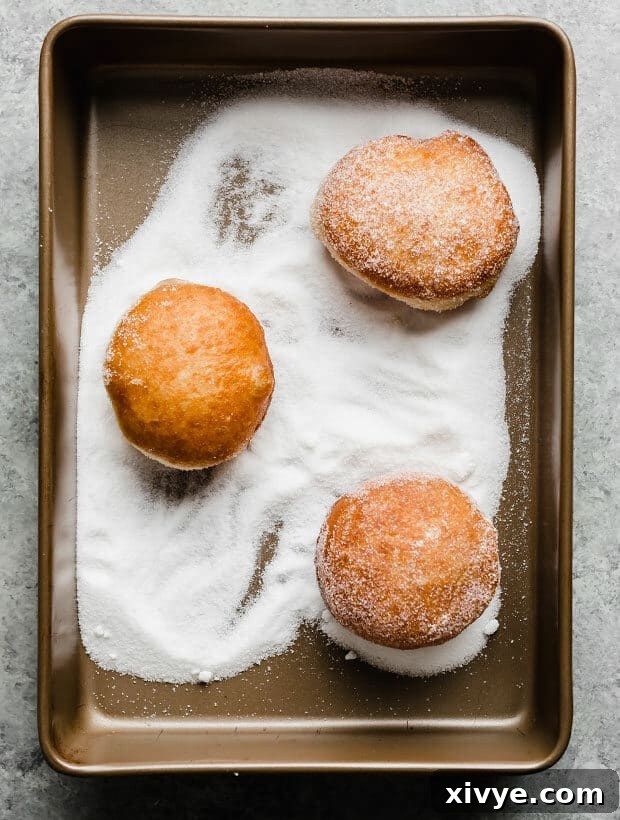 Three fried doughnuts being tossed in granulated sugar.