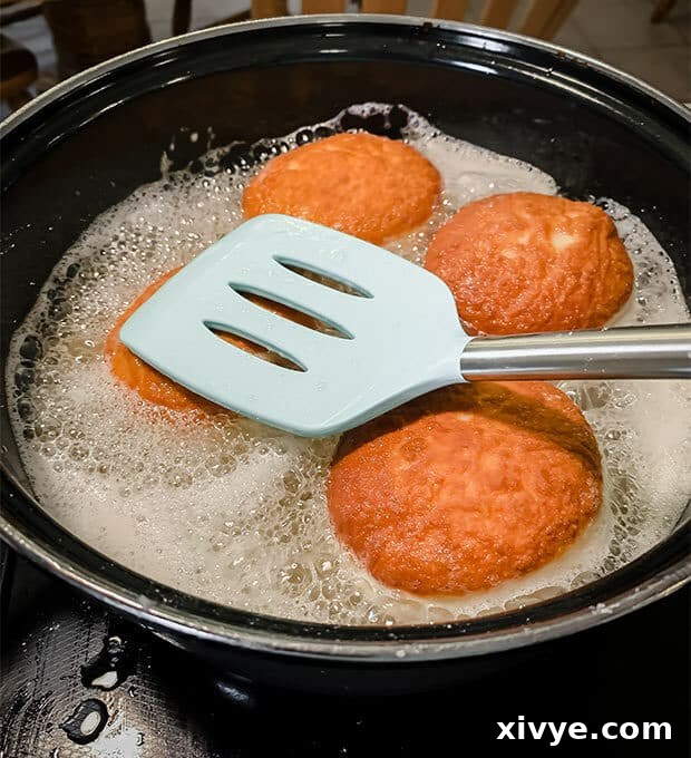 A spatula pushing down a doughnut in hot oil.