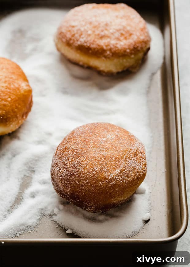A fried doughnut being tossed in granulated sugar.