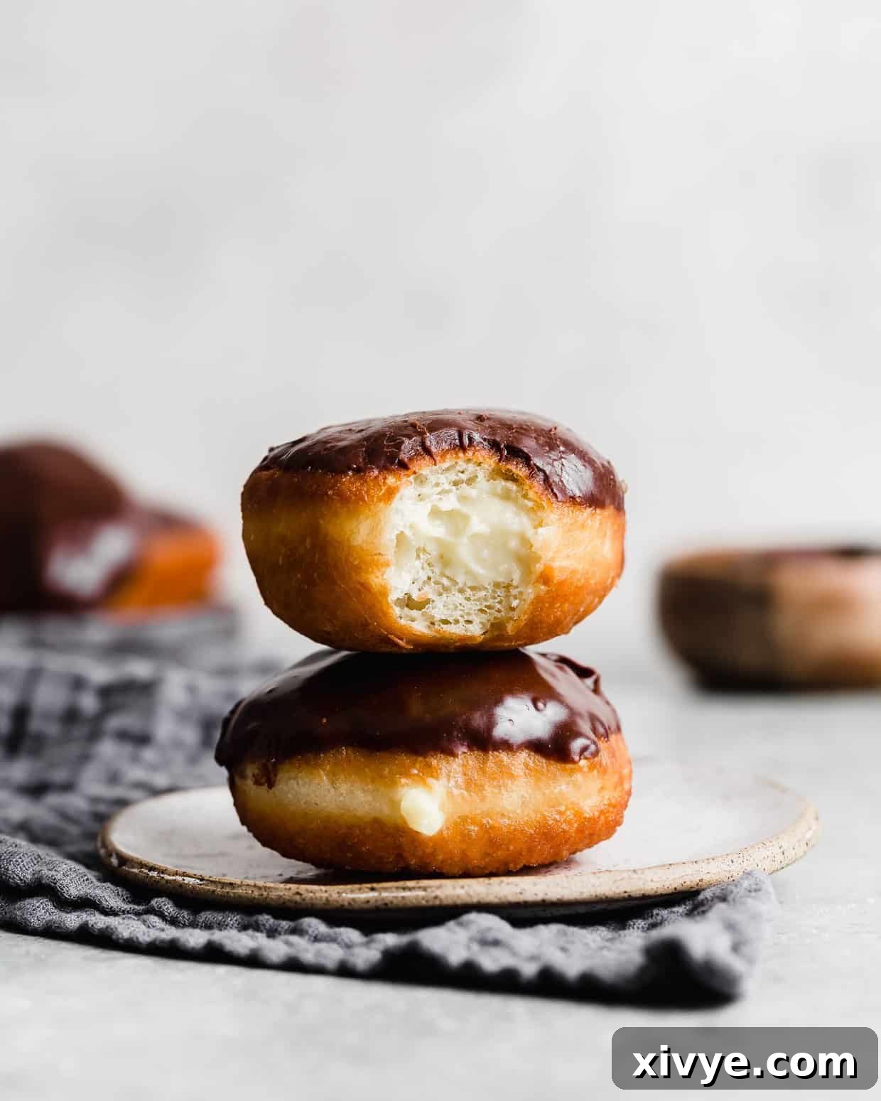 Perfect Homemade Boston Cream Donuts 2 Two Boston Cream Donuts stacked on top of each other, with the top donut having a bite taken out of it.