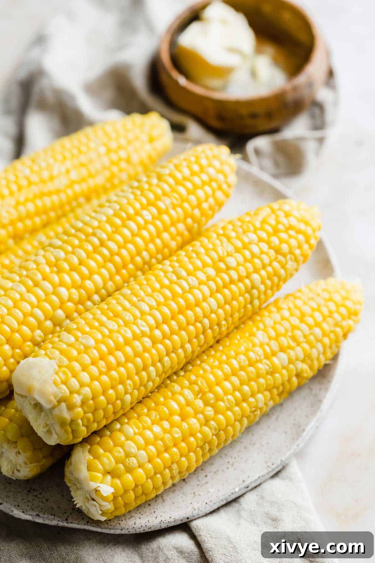 Perfectly boiled corn on a white plate with a bowl of butter in the background.