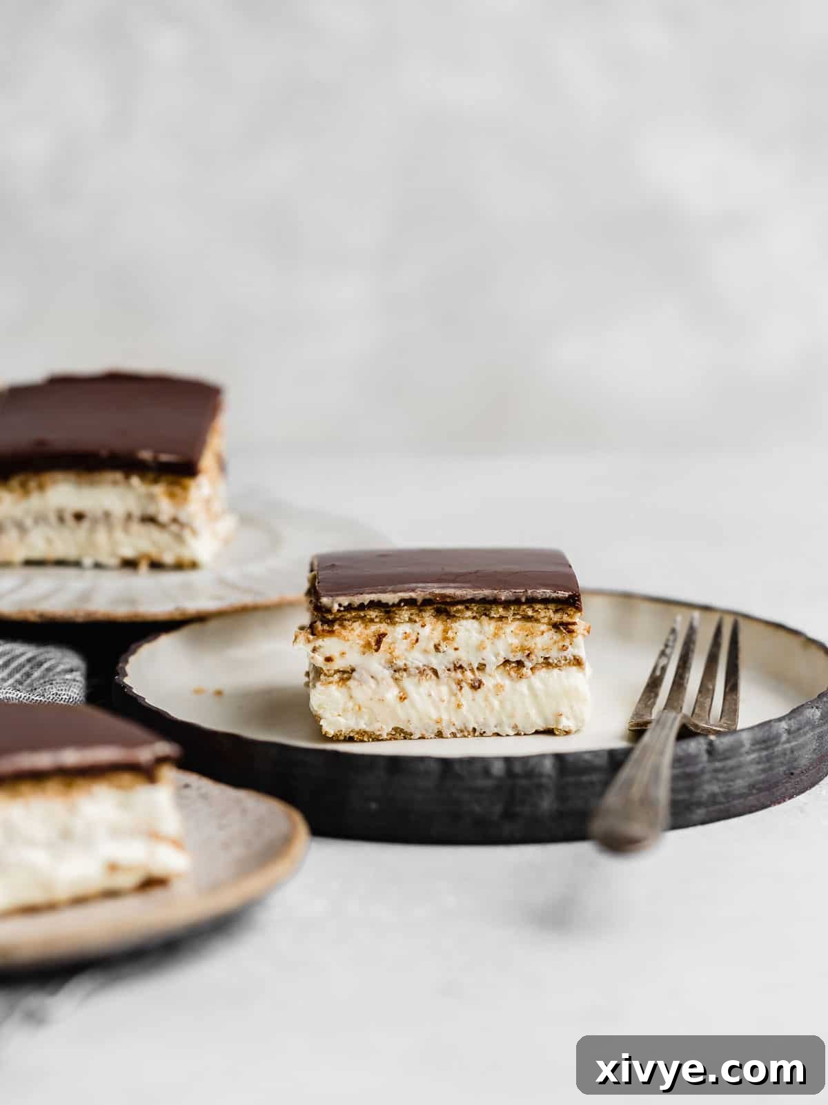 A perfectly sliced piece of Chocolate Eclair Cake on a white plate, showcasing its soft layers against a clean white background.