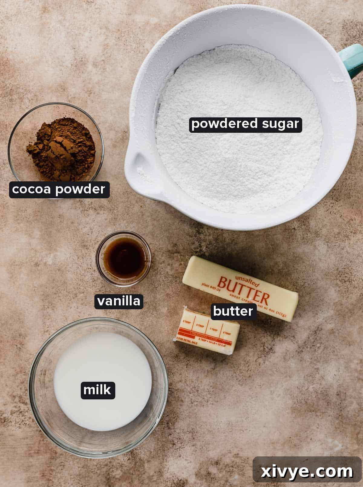 Texas Sheet Cake frosting ingredients on a light brown textured background, featuring butter, cocoa, milk, powdered sugar, and vanilla.