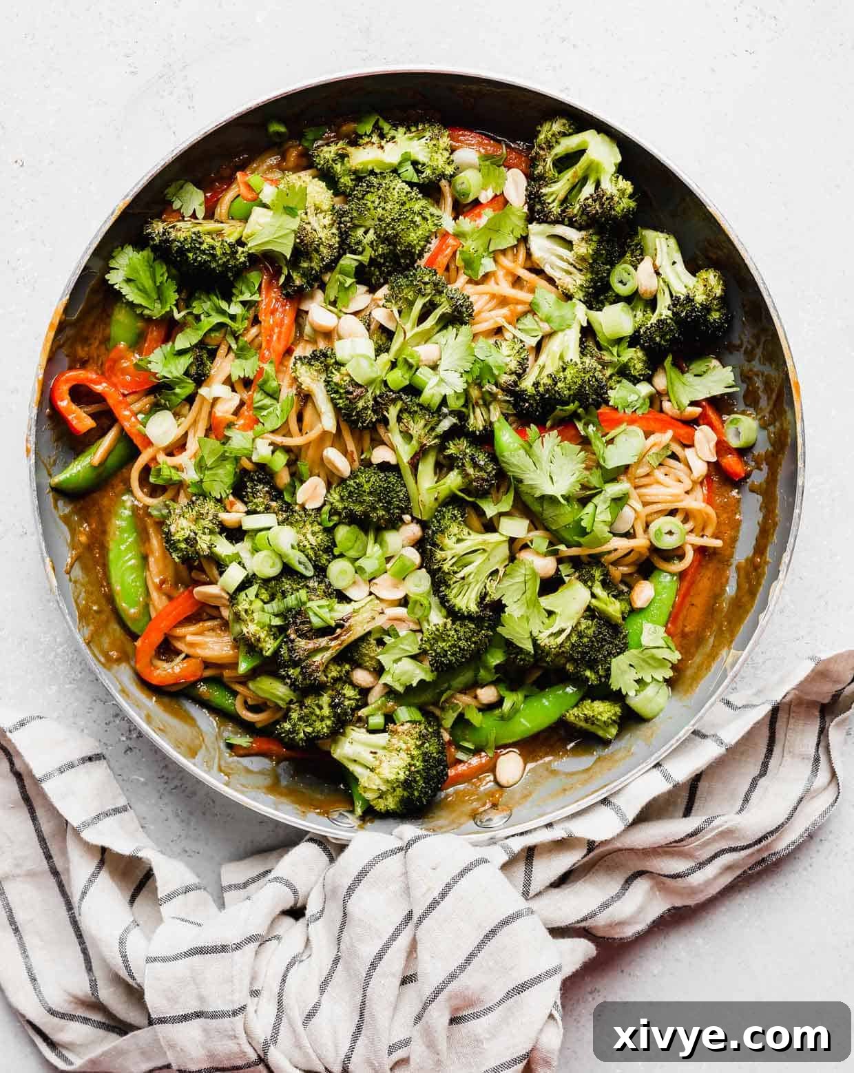 A gray skillet with Peanut Noodles with Vegetables in it on a white background.