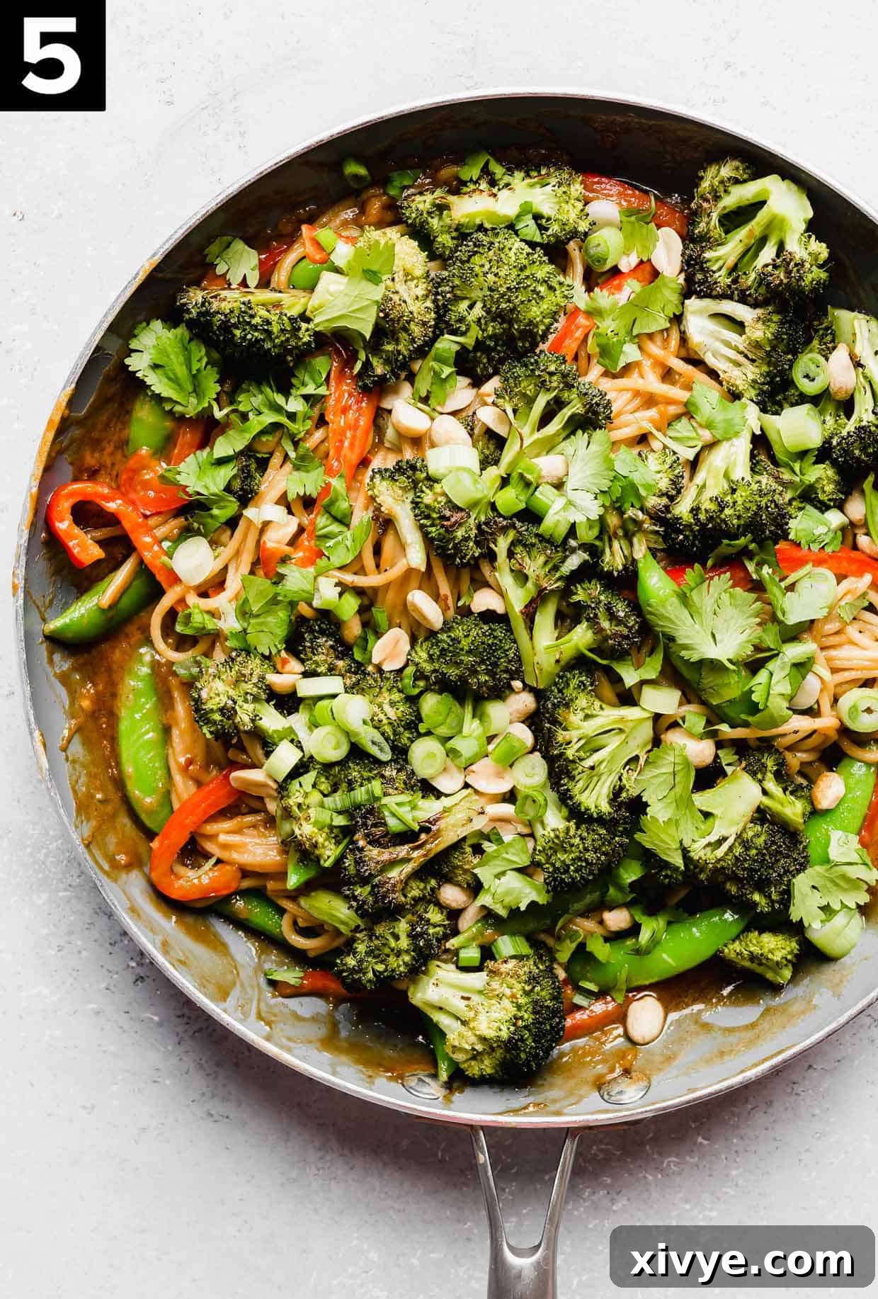 A skillet filled with roasted broccoli peanut butter noodles with vegetables.