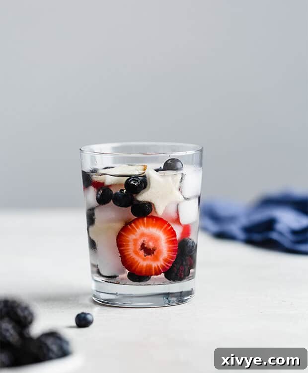A small glass of 4th of July fruit-infused water, showcasing sliced strawberries, plump blueberries, and dark blackberries swimming in clear, refreshing water.
