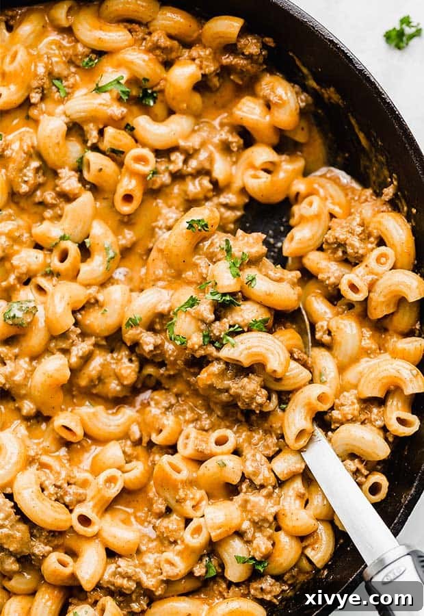 Ultimate Homemade Beef & Mac 2 A close up photo of macaroni noodles, seasoned ground beef, and a rich, creamy cheesy sauce in a cast iron skillet, garnished with fresh parsley.