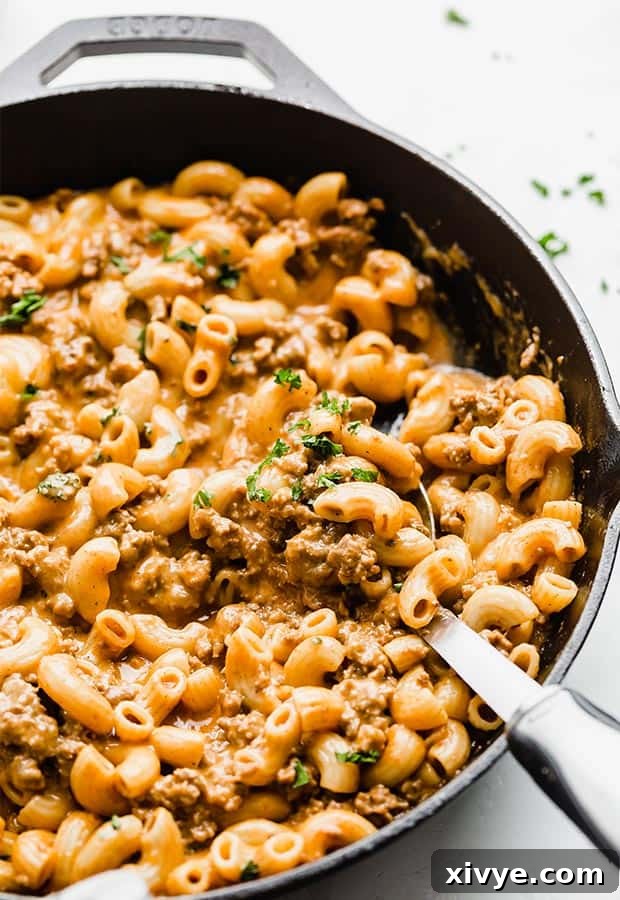Ultimate Homemade Beef & Mac 8 A large serving spoon scooping up a generous portion of homemade meat and cheese pasta from a cast iron skillet, highlighting its creamy texture.